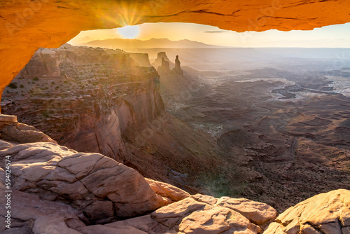 A phenomenal landscape scene of a rock opening with view of distance mountains and cliffs back illuminated by the rising sun  Mesa Arch at sunrise  Island In the Sky  Canyonlands  Utah