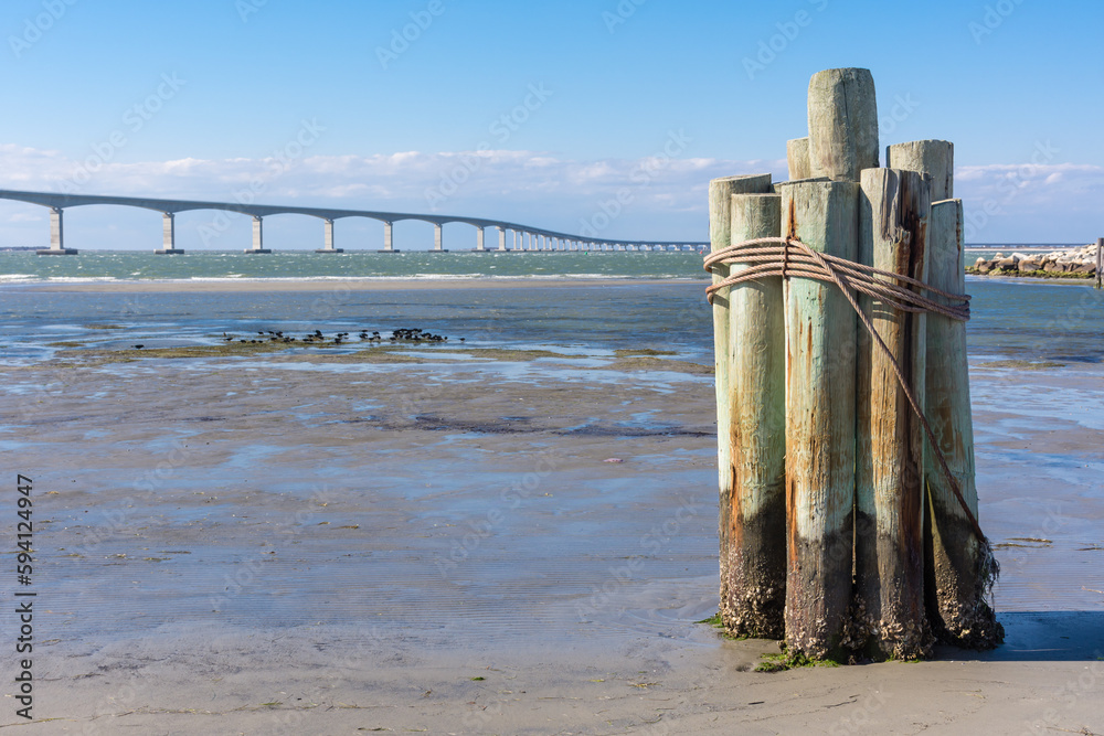 Close-up of bricoles at Oregon Inlet with Bonner Bridge in distance. Clouds and blue sky, full sun. Close-up of bricoles at Oregon Inlet with Bonner Bridge in distance. Clouds and blue sky, full sun.