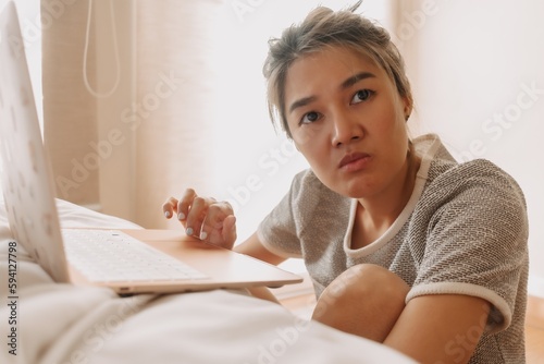 Serious asian woman working with her laptop in the bedroom.