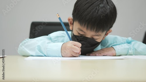 Asian boy wearing formal shirt and chemical face mask writing a test or exam for entering school.