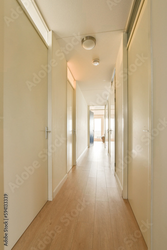 a long hallway with white walls and wood flooring on both sides  leading to an open door that leads to another room