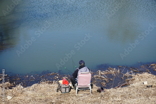 Fisherman sitting on a chair on the bank of a lake  