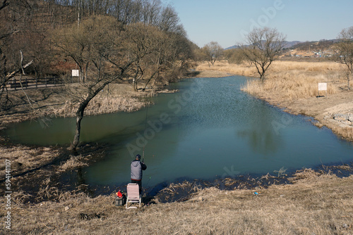 Fisherman sitting on a chair on the bank of a lake  