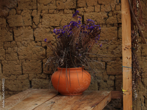 Jarrón de barro artesanal con flores sobre una mesa de madera, ornamento tradicional © AnaSofia