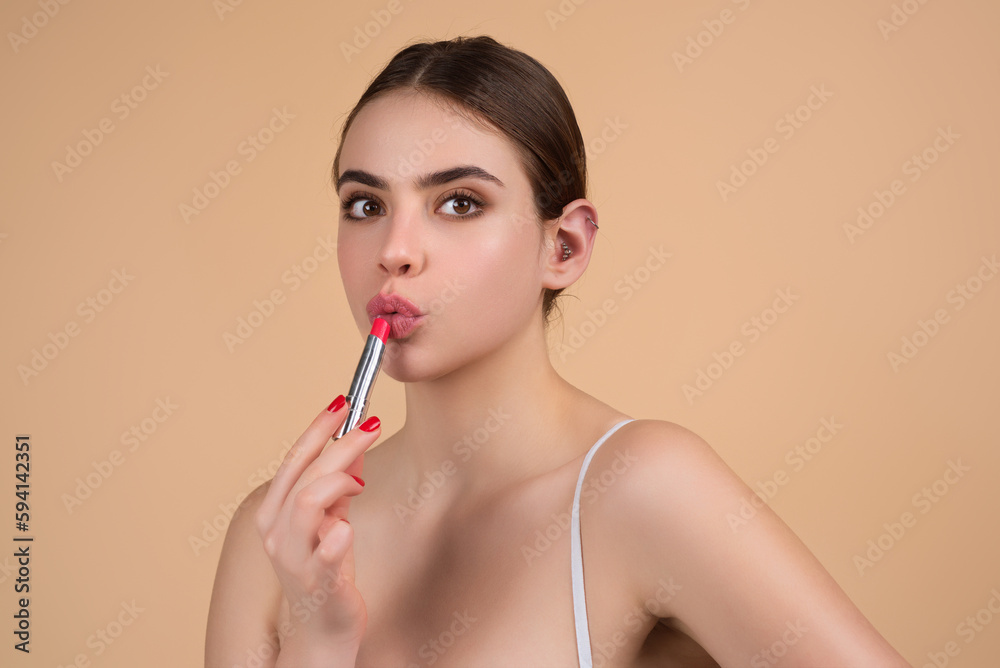 Gorgeous young woman in stylish makeup. Girl posing with new lipstick in studio. Sexy girl rouging her lips. Sexy model holding red lipstick. Applying lipstick cream balm to mouth. Red is trending. Gorgeous young woman in stylish makeup. Girl posing with new lipstick in studio. Sexy girl rouging her lips. Sexy model holding red lipstick. Applying lipstick cream balm to mouth. Red is trending.