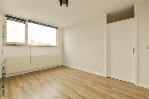 an empty room with wood flooring and white walls  there is a heater on the wall in front of the window