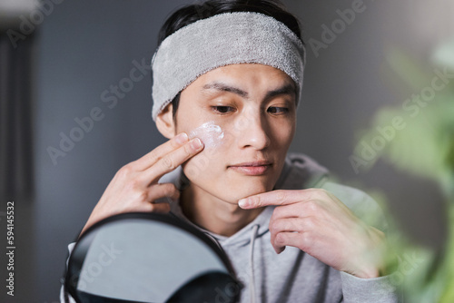 鏡を見ながらニキビの治療やニキビ跡のケアをしているクリームを頬に塗る若い男性 photo