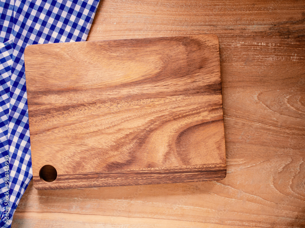 Empty cutting board on blue and white checkered fabric or napkin on rustic wood background.  Concept kitchen utensils and tableware. Mock-up, for food product. Top view, flat lay with copy space.