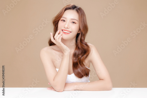 Young Asian beauty woman curly long hair with korean makeup style touch her face and perfect skin on isolated beige background. Facial treatment, Cosmetology, plastic surgery. photo
