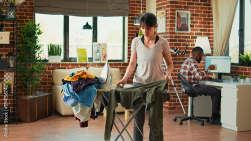 Female person ironing blouse in apartment after doing laundry, using steam iron to take out wrinkles on clothing. Young woman doing household chores, housekeeping weekend activity.