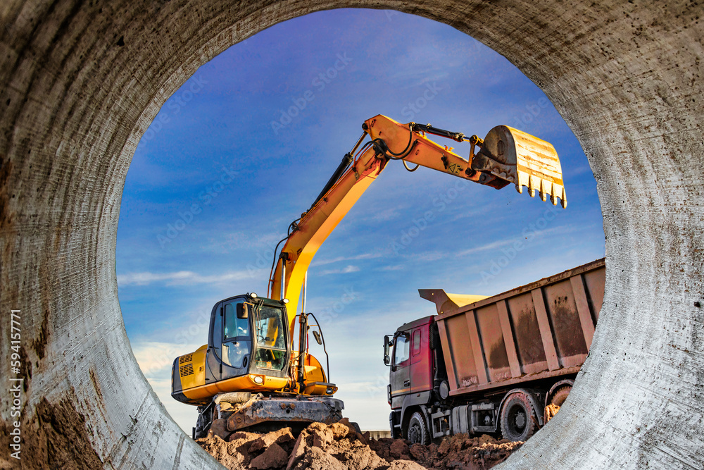 A wheeled excavator loads a dump truck with soil and sand. An excavator