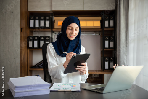Canvas Print Young Arabic female entrepreneur wearing a hijab working online with a laptop at office