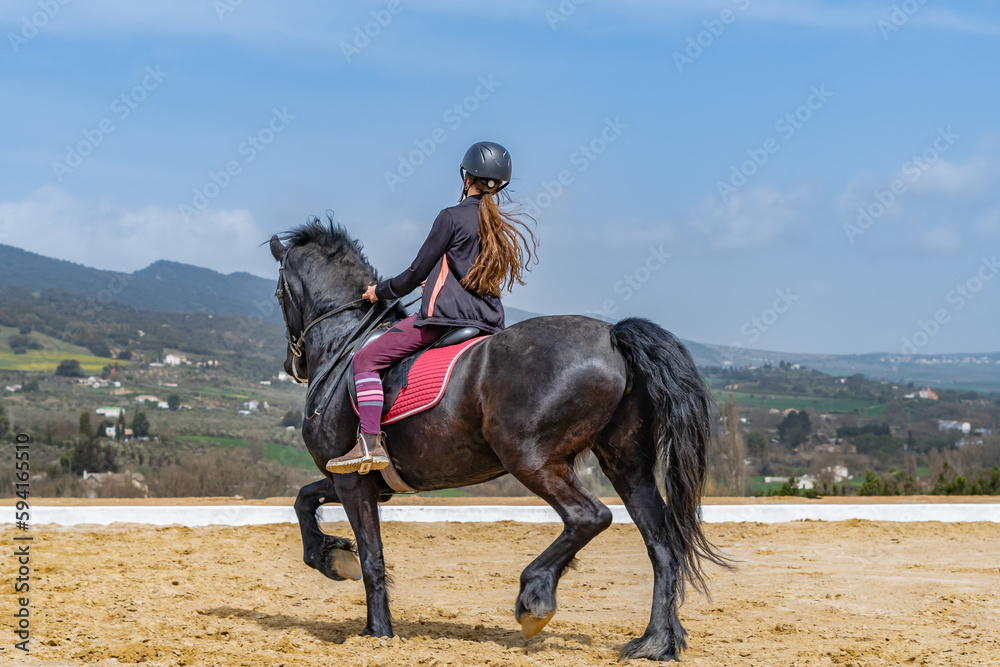 unrecognizable woman riding on a black horse with a mountainous landscape in the background and blue sky unrecognizable woman riding on a black horse with a mountainous landscape in the background and blue sky