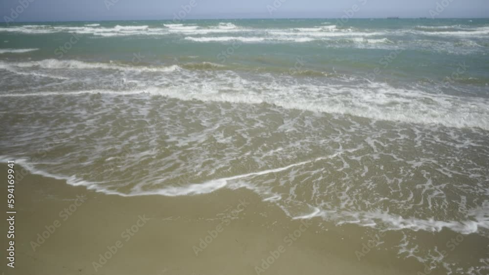 Sea surf on a sandy beach in spring. Beautiful clouds in the blue sky above the horizon. Waves crash on the sandy shore. Castellon, Spain Sea surf on a sandy beach in spring. Beautiful clouds in the blue sky above the horizon. Waves crash on the sandy shore. Castellon, Spain