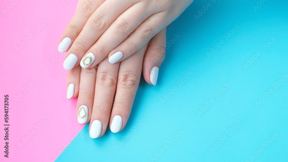 Female hands with white manicure on blue and pink background, top view. Female hands with white manicure on blue and pink background, top view.