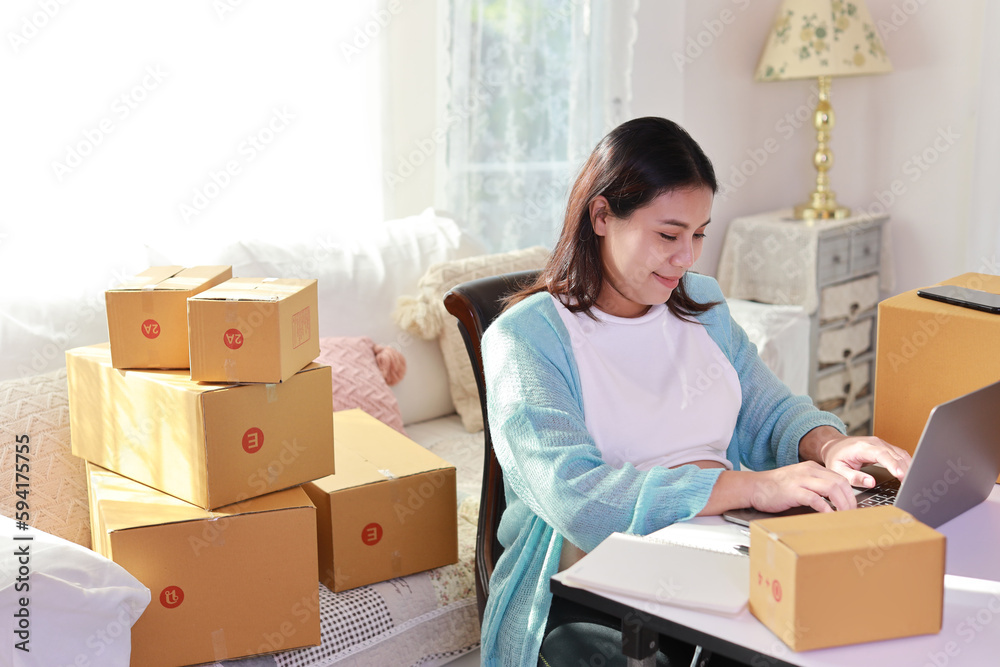 Attractive happy asian pregnant woman sitting and using mobile smart phone and making order for customer with computer. Expectant mother preparing and working for baby birth during pregnancy concept