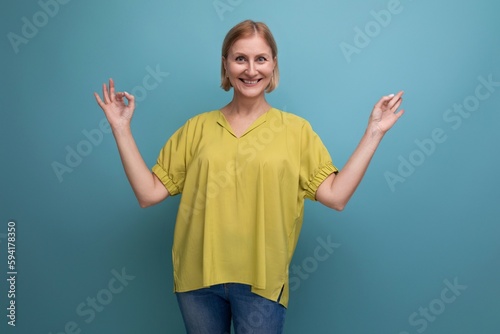 funny blond mature woman in yellow t-shirt having fun on studio background