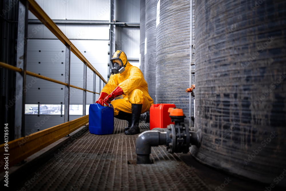 Industrial chemicals production. Experienced worker in protection suit, gas mask, gloves and boots opening canister with acid in zinc galvanizing factory. Industrial chemicals production. Experienced worker in protection suit, gas mask, gloves and boots opening canister with acid in zinc galvanizing factory.