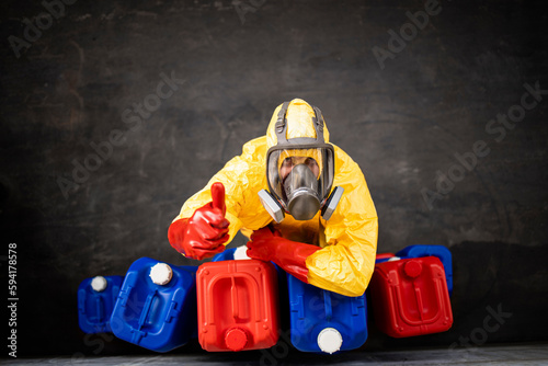 Top view of professional worker in chemical protection suit and gas mask standing by plastic canisters and holding thumbs up.