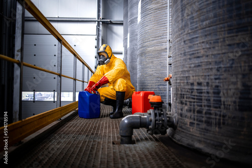 Industrial chemicals production. Experienced worker in protection suit, gas mask, gloves and boots opening canister with acid in zinc galvanizing factory.