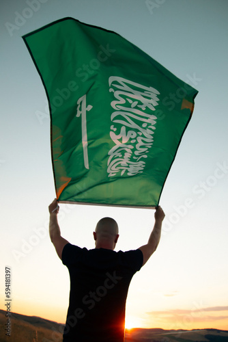 Man holding Saudi Arabia national flag waving in beautiful clouds. photo