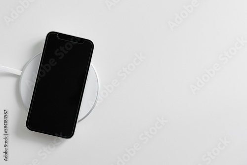 Black phone lying on white cordless charger with copy space