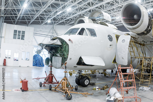 Close-up of white transport aircraft in the hangar. Airplane under maintenance. Checking mechanical systems for flight operations