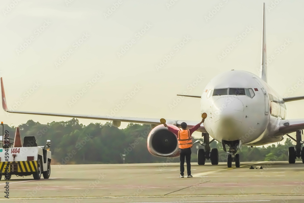 Naklejka premium Ground Crew in the signal vest. Aviation Marshall or Supervisor meets passenger airplane at the airport. Aircraft is taxiing to the parking place. Apron movement control officer in safety vest parking