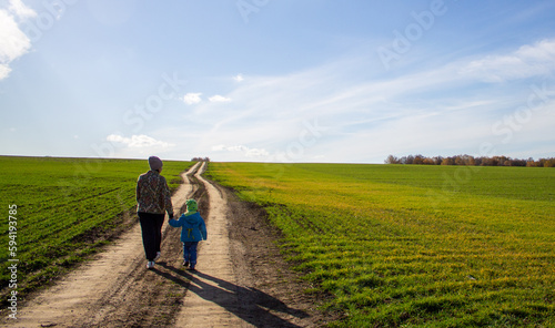 a woman with a child walk along the road in a green field