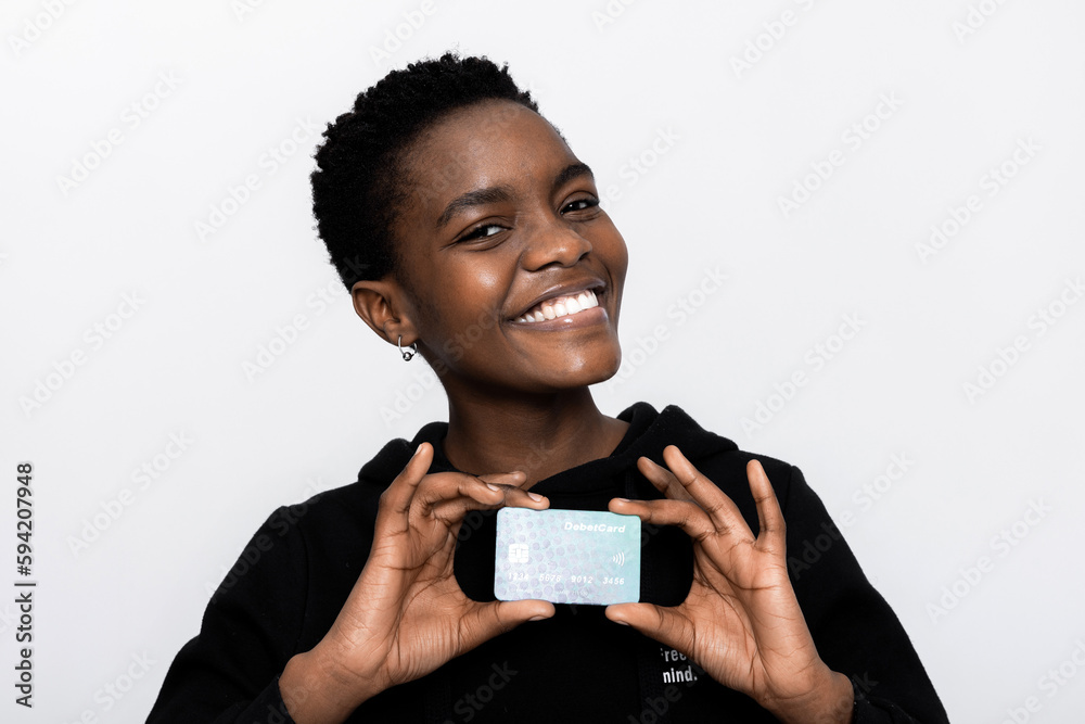 Delighted black african american woman in casual black hoodie smiling with white teeth at camera holding new modern credit card in hands standing over white background in studio isolated.Easy payment. Delighted black african american woman in casual black hoodie smiling with white teeth at camera holding new modern credit card in hands standing over white background in studio isolated.Easy payment.