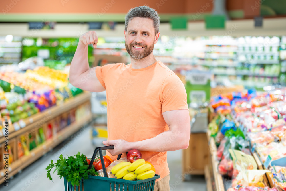Portrait of man with shopping cart full of fresh vegetables in a food store. Supermarket shopping and grocery shop concept. Guy buying grocery in supermarket hold shopping basket.