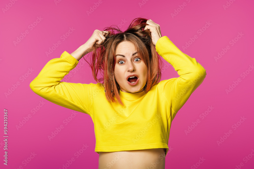 Portrait of a bothered woman dressed in yellow t-shirt pulling her hair out and screaming from regret, standing pink background Portrait of a bothered woman dressed in yellow t-shirt pulling her hair out and screaming from regret, standing pink background