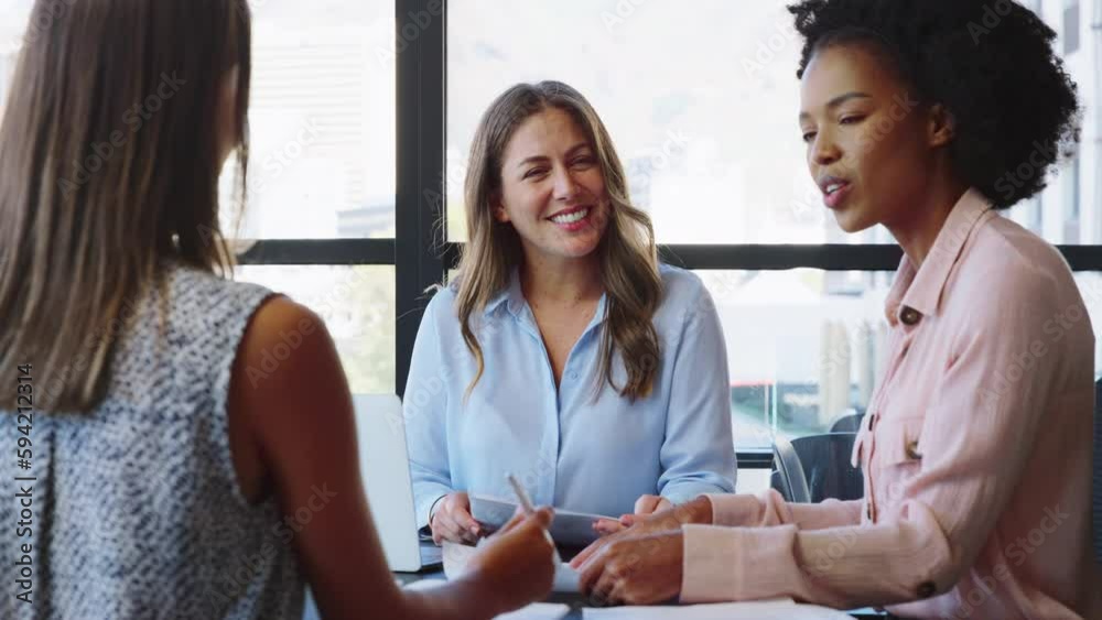 Female multi-cultural business team meeting around office boardroom table with laptops discussing documents - shot in slow motion Female multi-cultural business team meeting around office boardroom table with laptops discussing documents - shot in slow motion