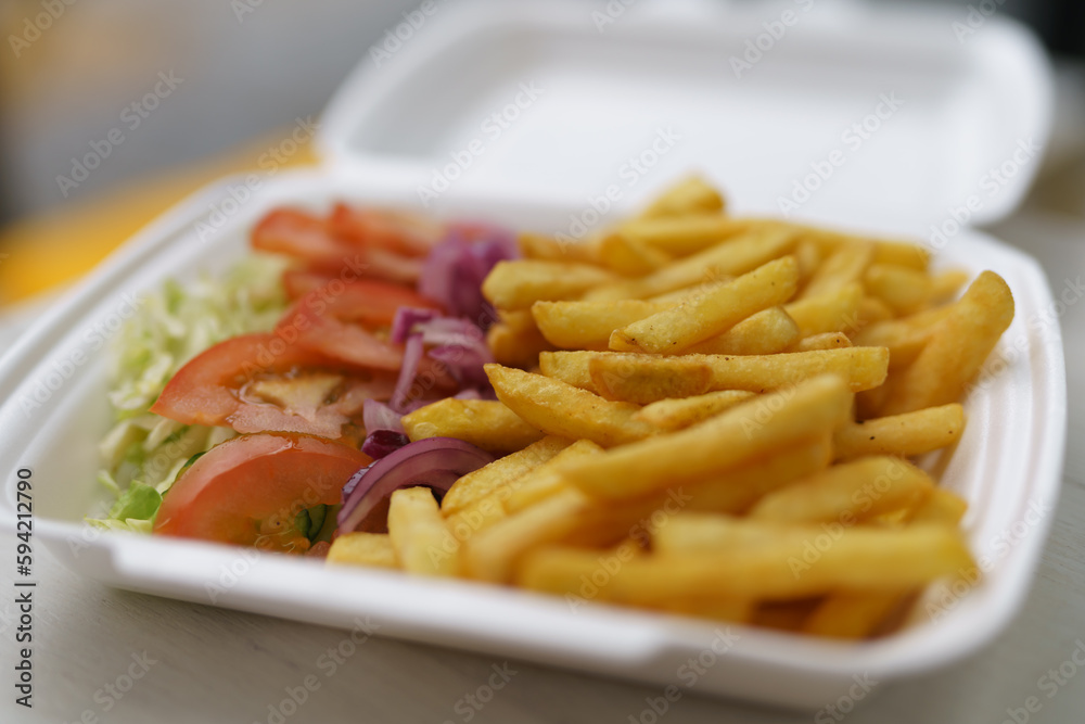 Stryrofoam lunch box with French fries and fresh vegetables. Traditional Greek kalamaki being prepared for take away