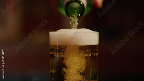 Pouring beer into glass in slowmo and rising foam flowing over