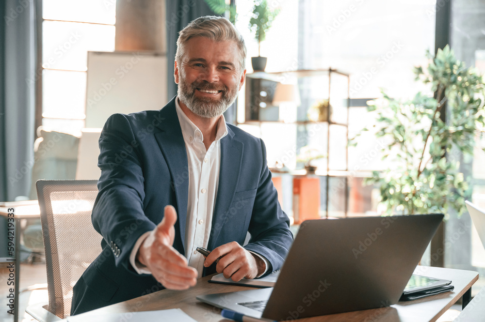 Smiling, giving hand to shake, greetings. Senior businessman is working in the office Smiling, giving hand to shake, greetings. Senior businessman is working in the office