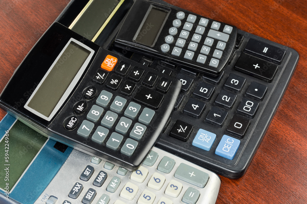 Different used electronic calculators stacked on wooden table, selective focus Different used electronic calculators stacked on wooden table, selective focus