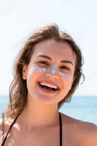 Beautiful young woman is posing at the camera with suncream on her face over the sea background
