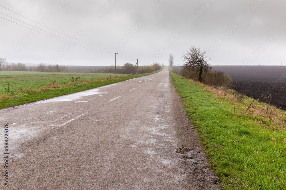 Rural asphalt road among the farmlands in overcast rainy day Rural asphalt road among the farmlands in overcast rainy day