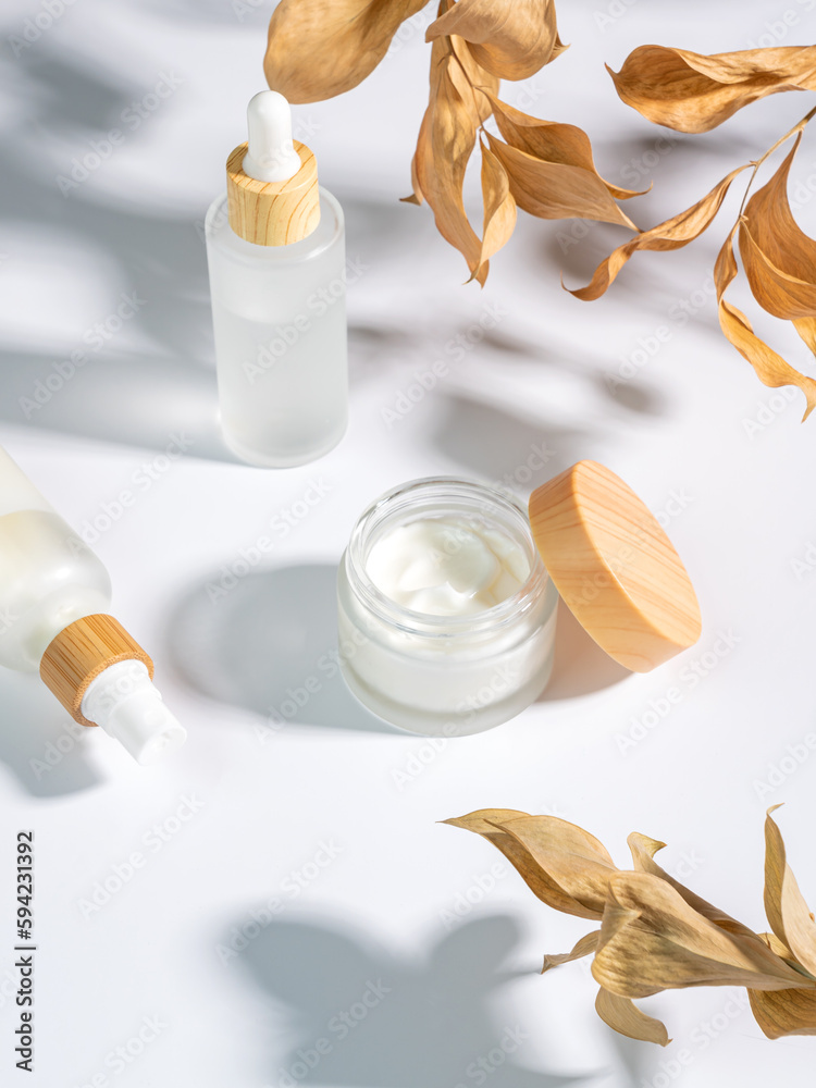 close up of collagen cream in glass jar, serum in white matte glass bottle and dry ruskus leaves on white background. Set for skin and body care beauty products close up of collagen cream in glass jar, serum in white matte glass bottle and dry ruskus leaves on white background. Set for skin and body care beauty products