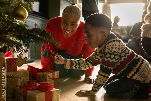 Mother and son looking at Christmas tree decorations with multi generational family celebrating