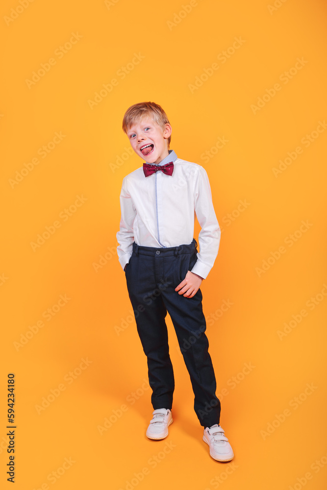 Full body portrait of smiling little boy in shirt with bowtie posing studio on yellow background Full body portrait of smiling little boy in shirt with bowtie posing studio on yellow background