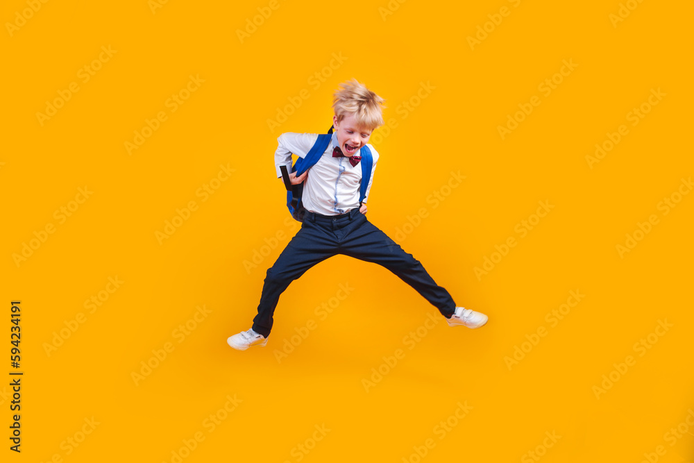 Little school boy student jumpsing high like a super hero on yellow background