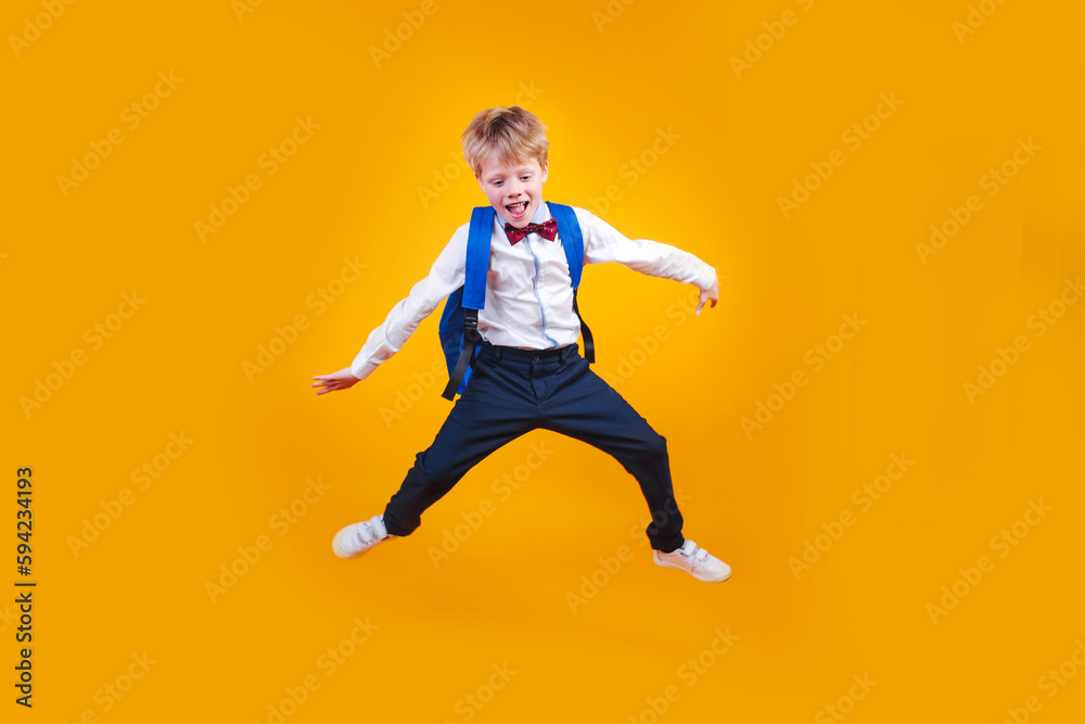 Full length shot of a boy with a backpack jumping on yellow background