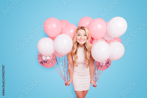 Portrait of positive elegant girlfriend in white dress having many white air balloons around her looking at camera isolated on pink background