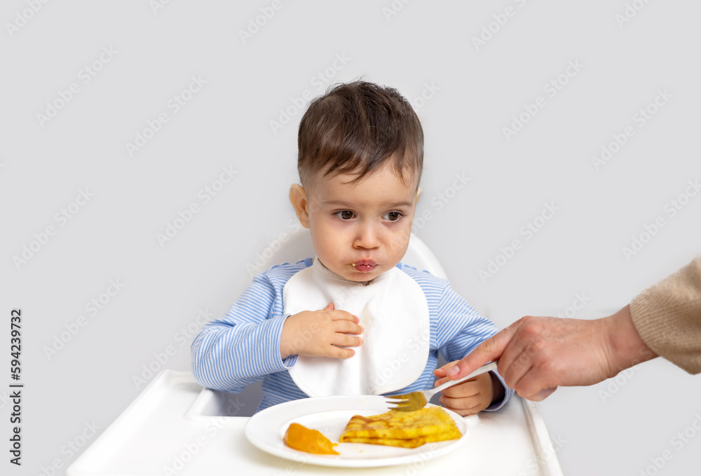 adorable baby boy kid eating peach pancake,mother hand feeding child. wide open mouth hungry cute boy with white bib modern kitchen home house interior.isolated infant food diversification high adorable baby boy kid eating peach pancake,mother hand feeding child. wide open mouth hungry cute boy with white bib modern kitchen home house interior.isolated infant food diversification high