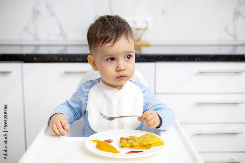 adorable baby boy kid eating peach pancake,mother hand feeding child. wide open mouth hungry cute boy with white bib modern kitchen home house interior.isolated infant food diversification high