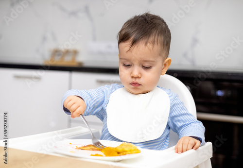 adorable baby boy kid eating peach pancake,mother hand feeding child. wide open mouth hungry cute boy with white bib modern kitchen home house interior.isolated infant food diversification high