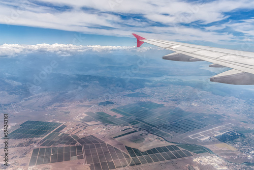 Airplane wing against the backdrop of a rural landscape with rectangular plots of land in Montenegro. View from the airplane window on the coastline of the Adriatic Sea in the Balkans