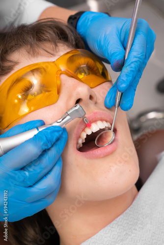Female dentist removes tartar from her teeth.Visit is carried out in a professional dental clinic. Woman is sitting on a dental chair.Drilling and treatment of the tooth, filling. Vertical photography
